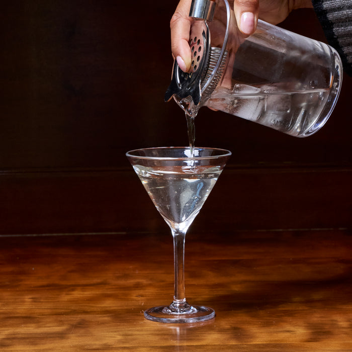 Liquid being poured from a cocktail shaker into a martini glass with strainer attachment.