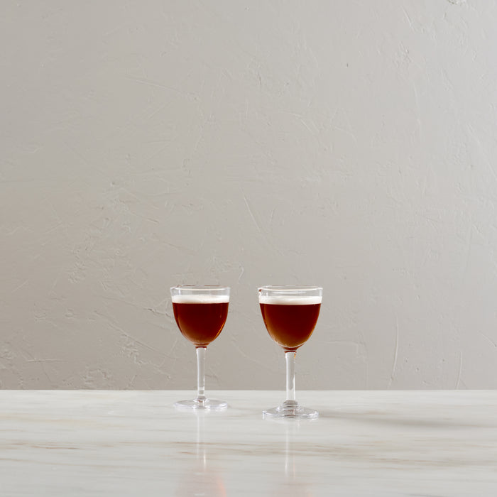 Two clear Nick & Nora glasses filled with red liquid, displayed side by side on a white surface.