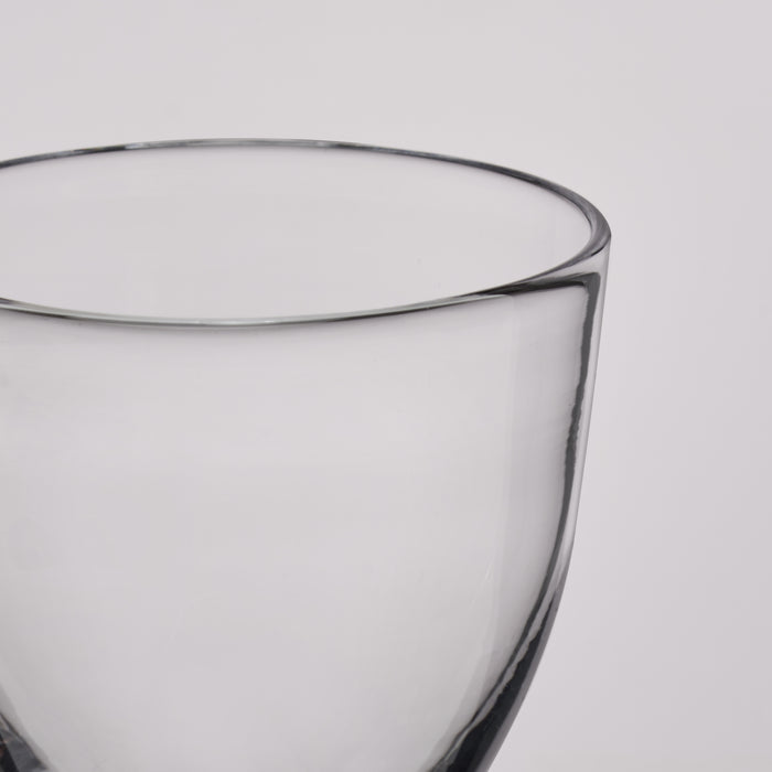 Clear glass coupe with curved bowl and dark rim, shown in close-up detail.