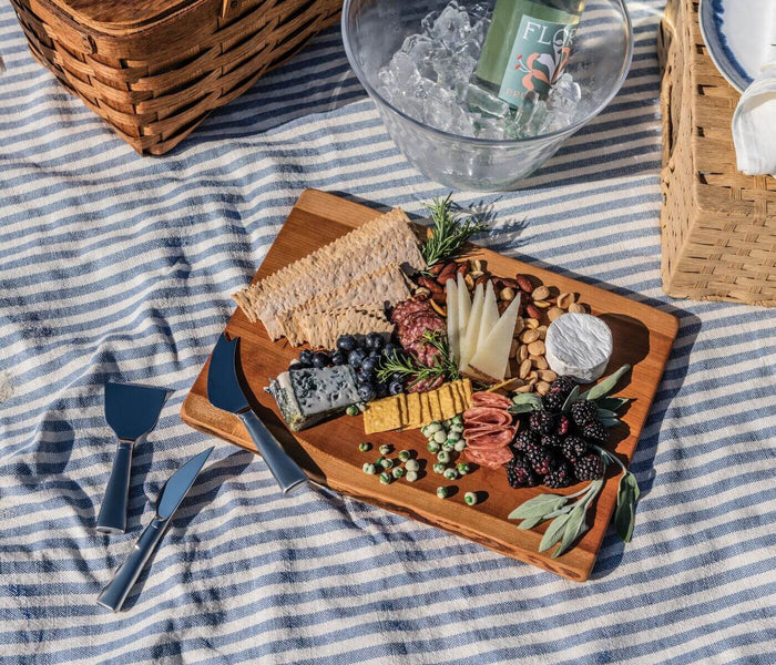 Cherry wood serving board with curved live edges, arranged with cheeses, cured meats, nuts, and fresh garnishes.