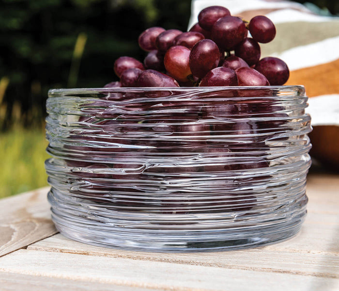 Clear glass bowl with horizontal ribbed texture containing red grapes.