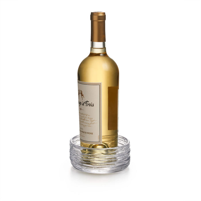 White wine bottle with cream and gold label sitting in a clear glass coaster with concentric circular ridges.