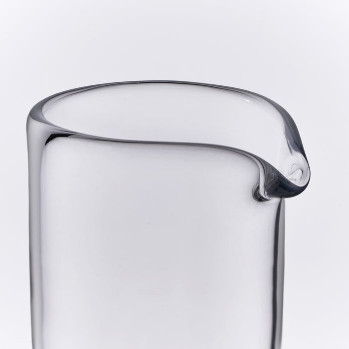 Clear glass carafe with curved pouring spout and rounded rim against white background.