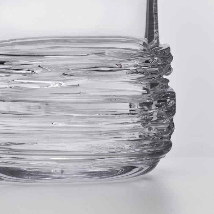 Clear glass decanter with wavy textured body and a tall dark stem on white background.