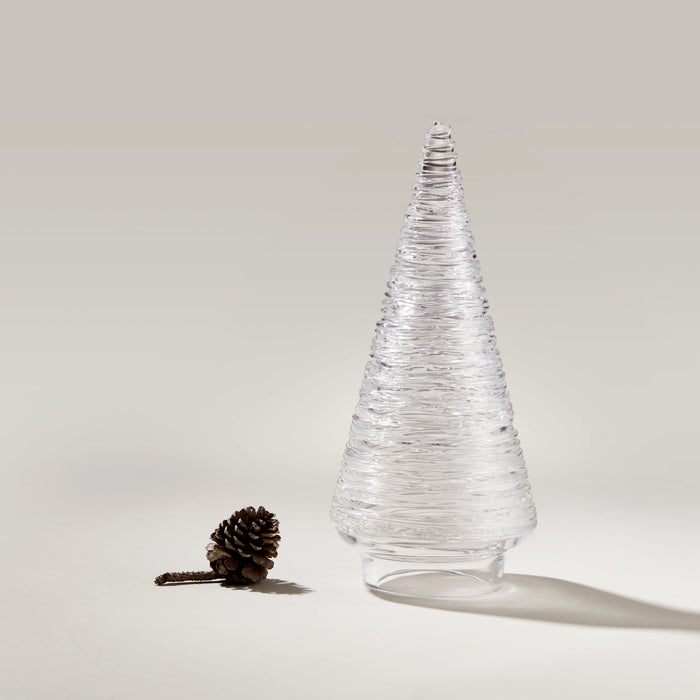 Clear glass cone-shaped decorative tree with textured surface and pinecone beside it on white background.