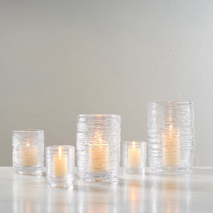 Five clear glass hurricane candles with textured surfaces and lit flames in varying heights arranged in a group.