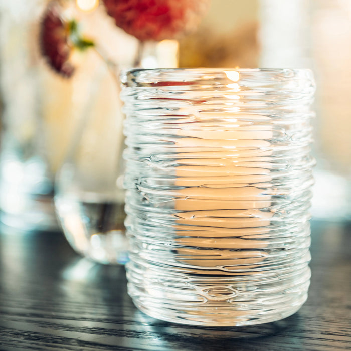 Clear glass hurricane candle holder with horizontal ribbed texture and warm light glowing inside.