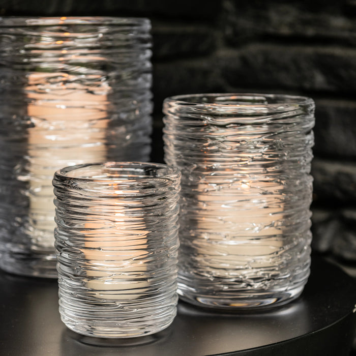 Three clear glass hurricane candles with textured swirl pattern, lit with warm flames inside.