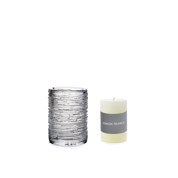 Cream pillar candle with gray band label next to textured glass hurricane holder.