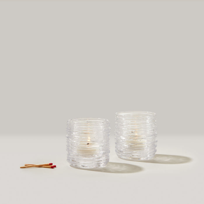 Two clear glass tealight candles with cream-colored wax and two wooden matches with red tips on neutral background.