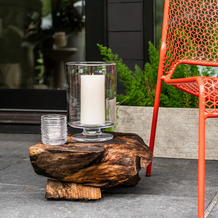 Cylindrical glass tealight holder with white candle on weathered wood base in outdoor patio setting.