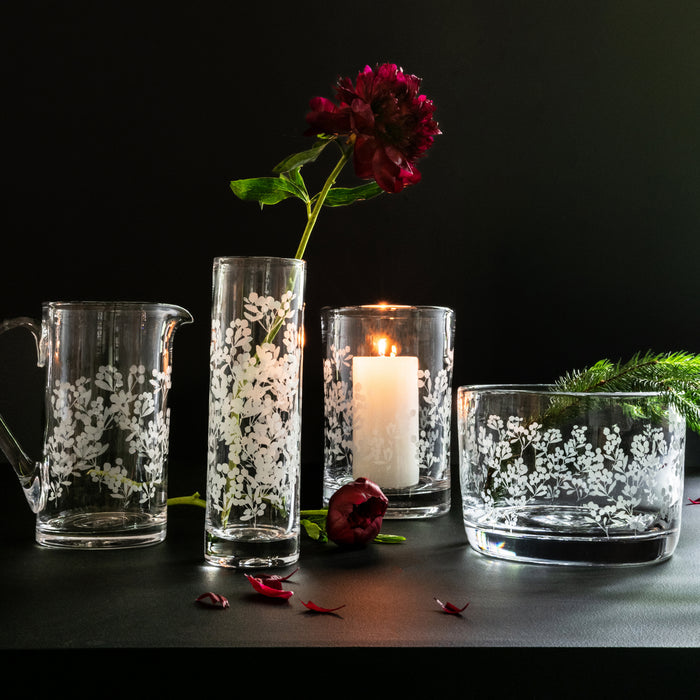 Large clear glass hurricane vase with white berry and leaf engraving, holding red flower with green stem.