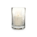 Clear glass hurricane candle with evergreen tree engraving and lit cream-colored candle inside.