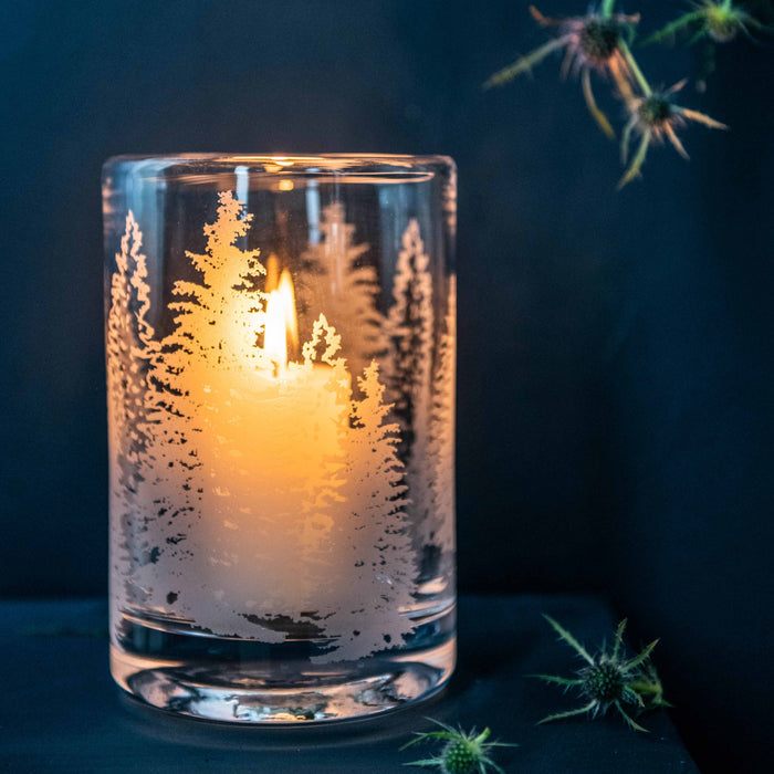 Clear hurricane candle holder with gold evergreen tree engraving, lit candle inside, medium size.