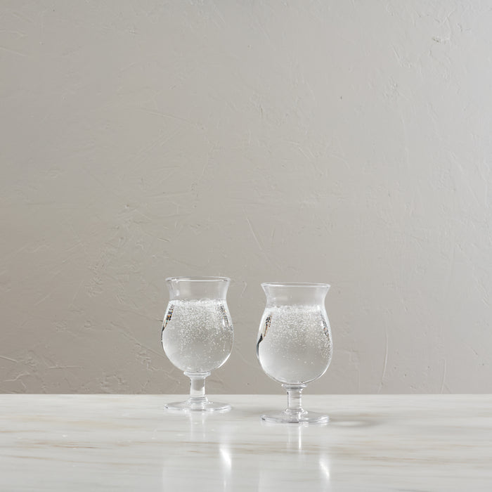 Two clear tulip-shaped glasses filled with water and ice on a white surface.