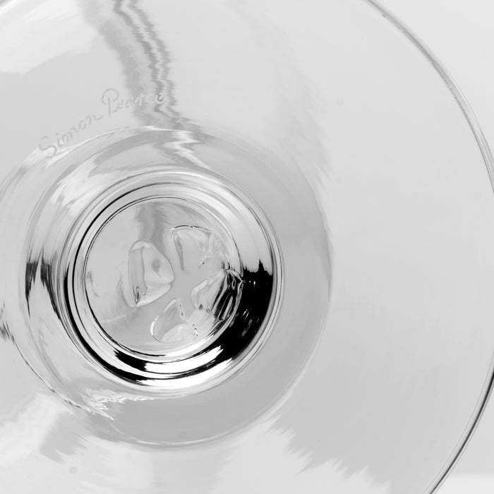 Close-up of a clear glass drinking glass, showing the base and a faint etched 'Simon Pearce' brand mark on the left side.