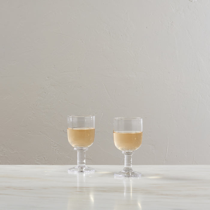 Two glasses filled with pale golden wine on a white surface against a light gray textured background.