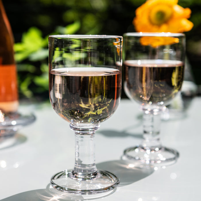Two wine glasses filled with white wine on outdoor table with garden background.