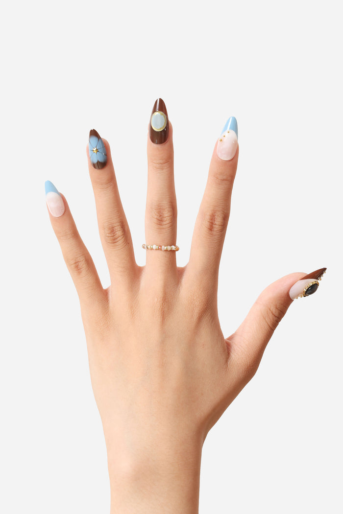 Almond press-on nails with blue, brown, and white designs, featuring floral and gold embellishments.