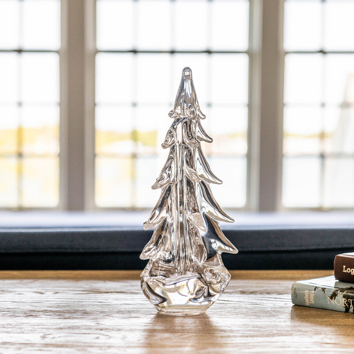 Clear glass evergreen tree decoration with tiered branches and pointed top sitting on wooden surface.