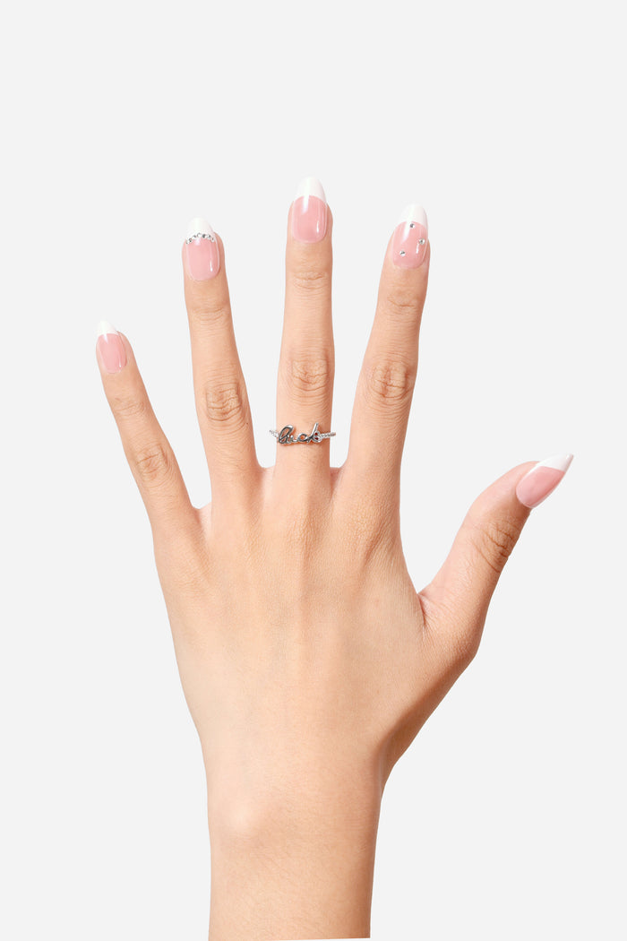 Short almond press-on nails with French tips and rhinestone accents, and a silver 'fuck' ring with rhinestones.