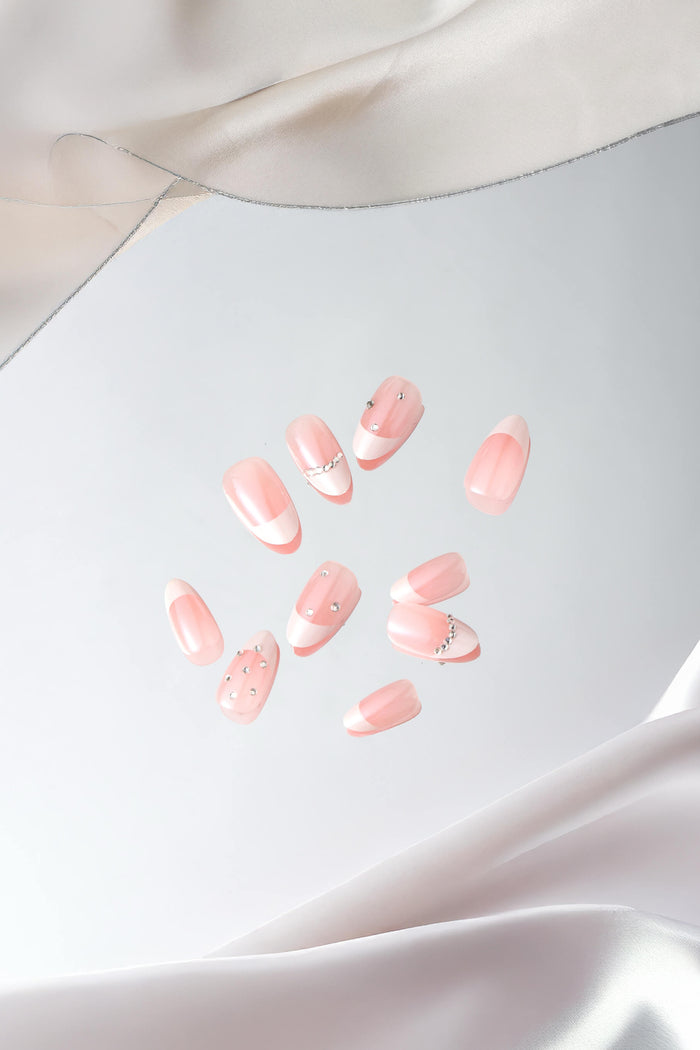 Short almond press-on nails with French tip design and rhinestone accents, set against flowing satin fabric.