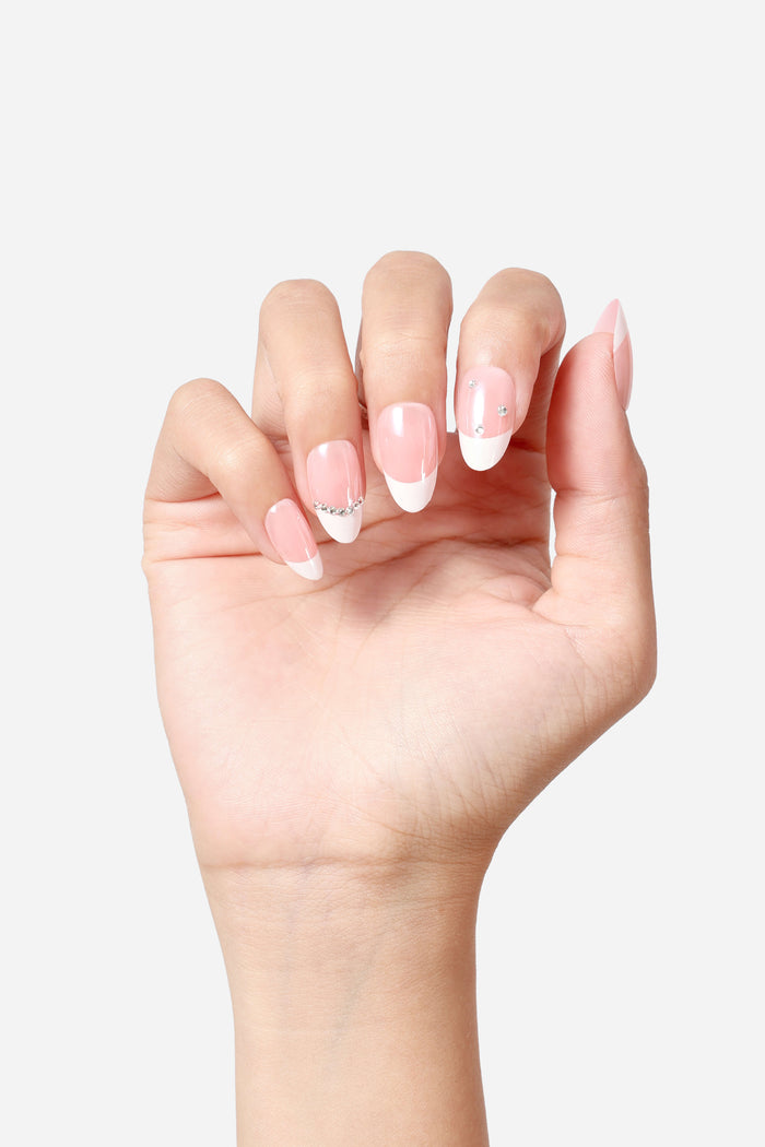 Short almond French press-on nails with subtle pink base, white tips, and rhinestone accents.