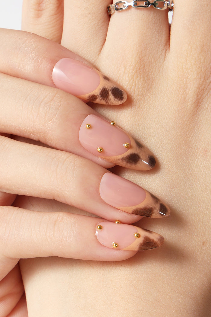 French tip press-on nails with leopard print and gold studs on a hand with a silver ring.