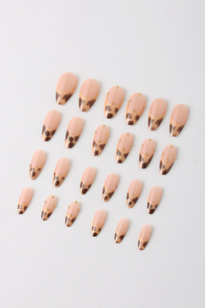 Nude oval press-on nails with leopard print French tips and gold stud accents.