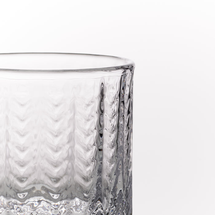 A close-up of a clear textured glass tumbler on a plain white background.