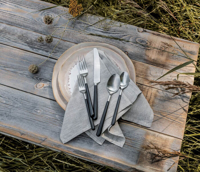 Five-piece flatware setting with fork, knife, and two spoons arranged on gray napkin and plate.