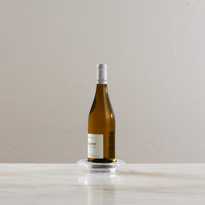 Clear glass coaster holding a wine bottle on a white marble surface.