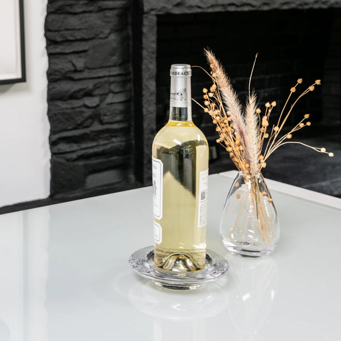 Clear glass coaster with decorative ridged border, holding white wine bottle on white surface.