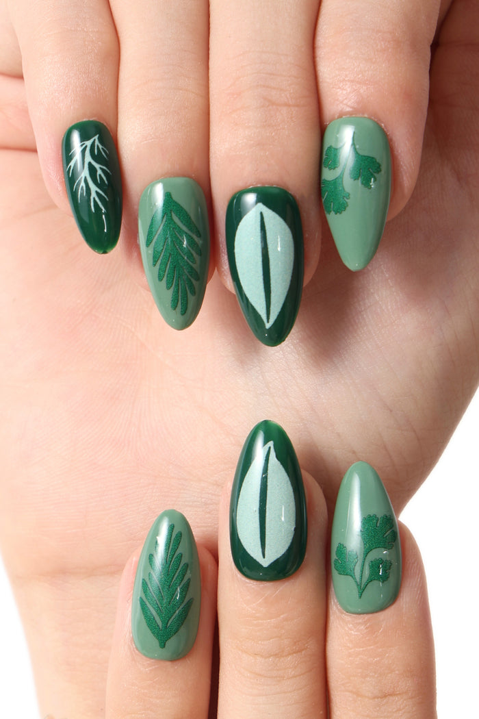 Green press-on nails with various botanical leaf designs, including fern fronds and abstract leaf shapes.