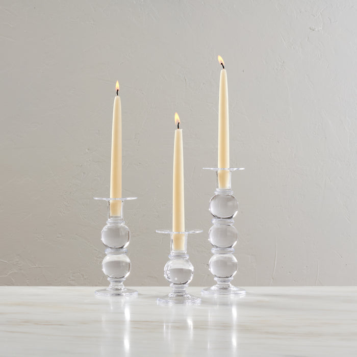 Set of three clear glass candlesticks with stacked spherical bases holding lit cream taper candles.