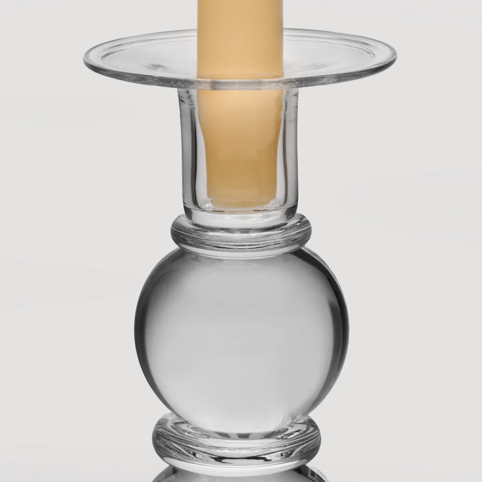 Clear glass candlestick with spherical base, cylindrical middle section, and wide circular top holding a cream pillar candle.