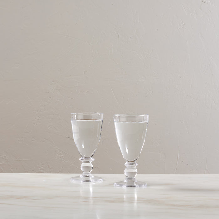 Two clear glass water glasses with pedestal bases filled with water, displayed side by side.