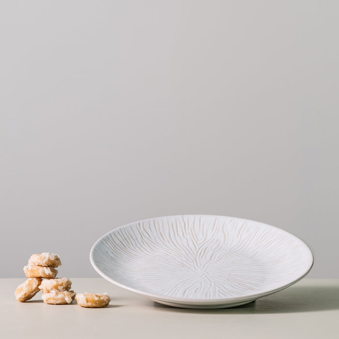 White ceramic platter with radial line texture pattern and small baked crackers beside it.