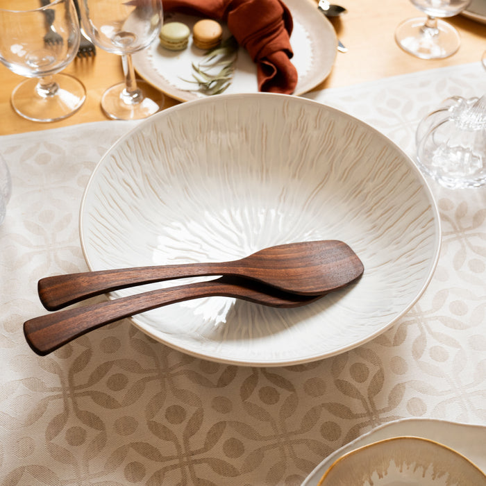 White ceramic serving bowl with radial texture pattern and two wooden serving utensils inside.