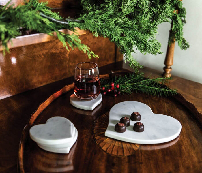 White marble heart-shaped board displayed on wooden table with glass and chocolates.