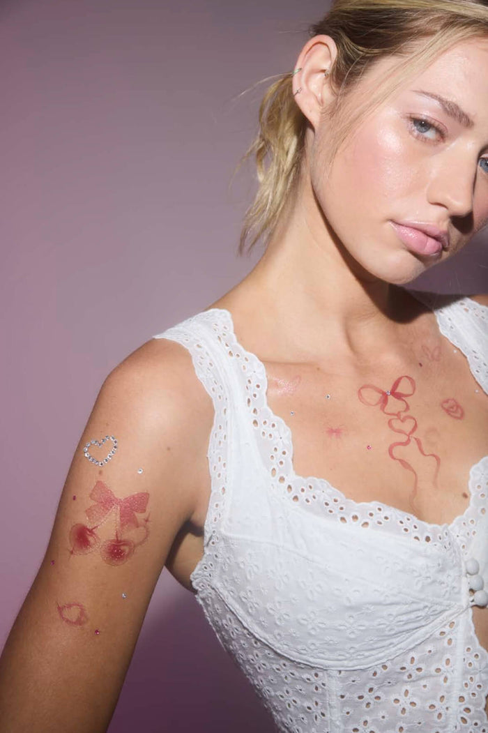 Woman with temporary Y2K tattoos: cherries, bows, hearts, and rhinestones on her arm and chest.