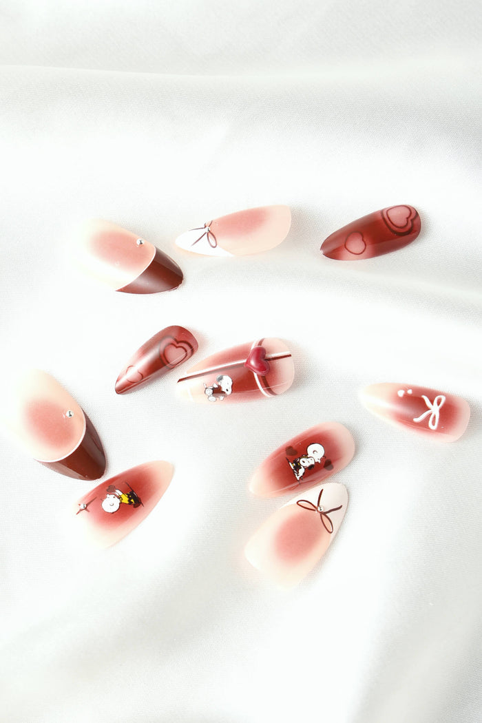 Almond press-on nails with Snoopy and heart designs in red and pink gradients.