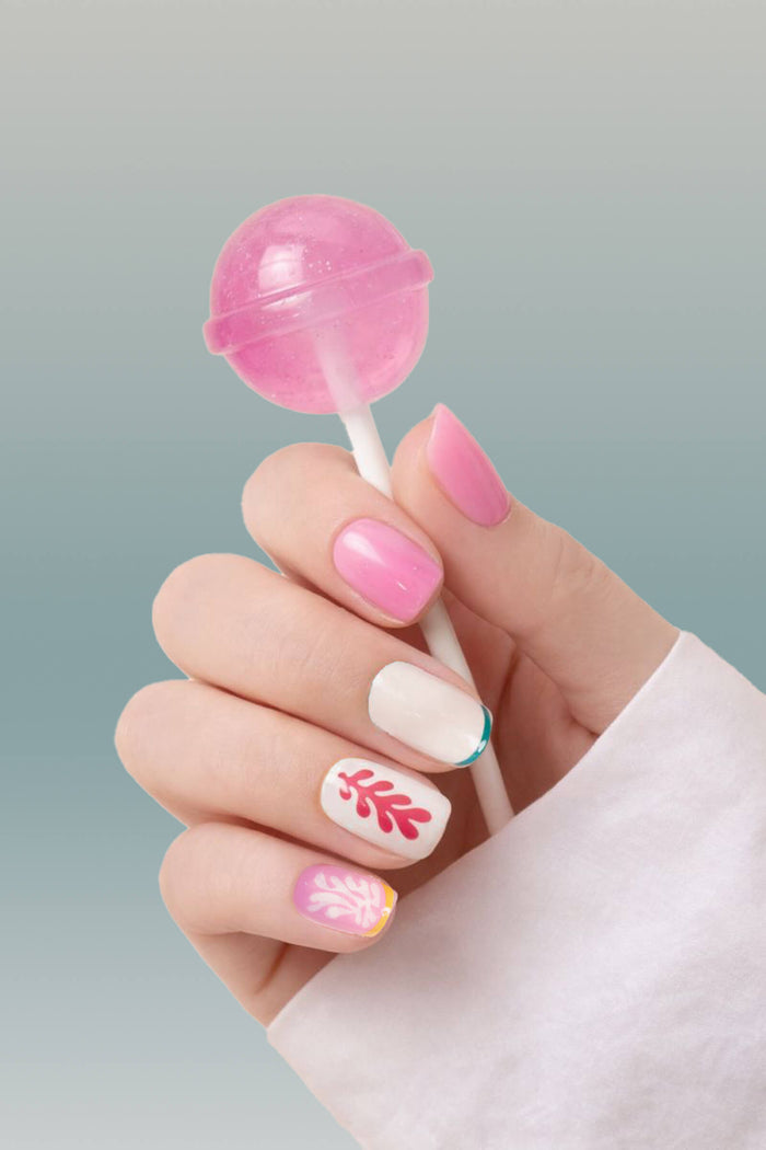 Hand holding a pink lollipop with square press-on nails featuring floral and leaf designs.