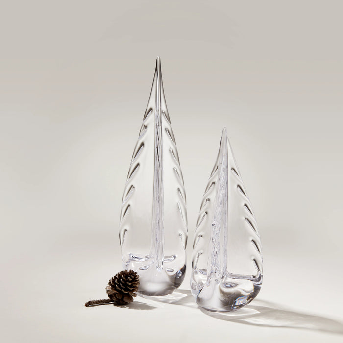 Two clear glass evergreen tree figurines with ice-like texture, alongside a small pinecone on neutral background.