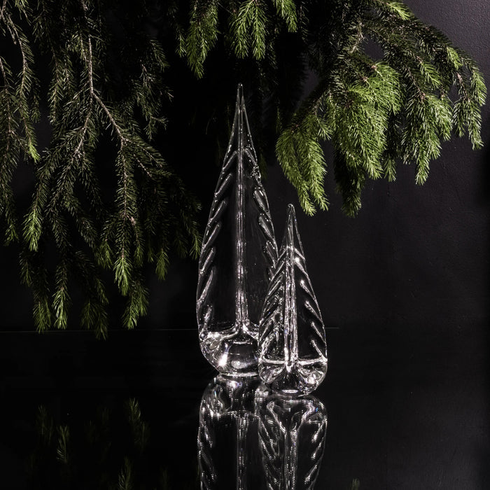 Frost-covered glass tree ornament with pointed spire beneath evergreen branches against dark background.