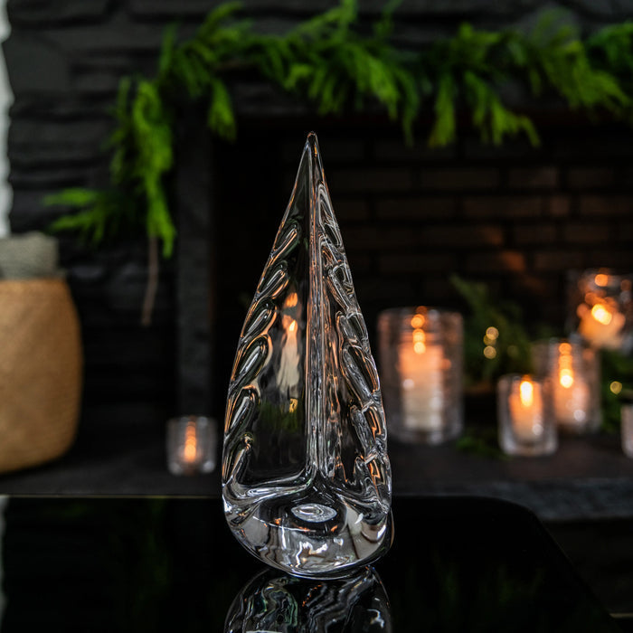 Clear glass teardrop-shaped candle holder with textured sides, displayed with lit candles and evergreen branches in backgroun