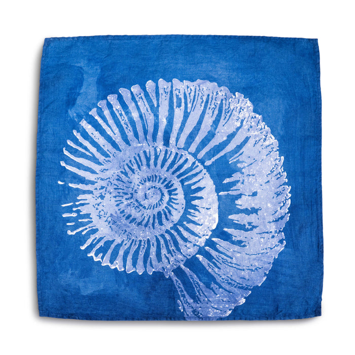 Indigo linen napkin featuring a white shell illustration with radiating ridges on a solid blue background.
