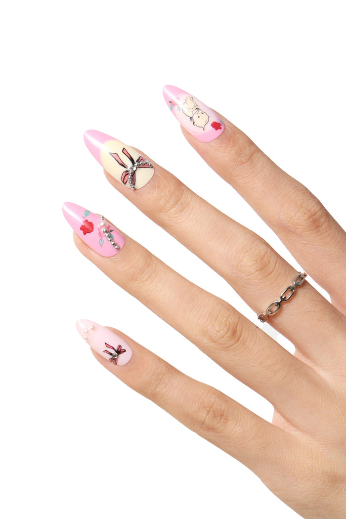 Pink almond press-on nails with playful Kewpie character designs and rhinestone accents.