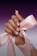 Short almond press-on nails with black lace French tips and pink bows, adorned with silver chain rings.