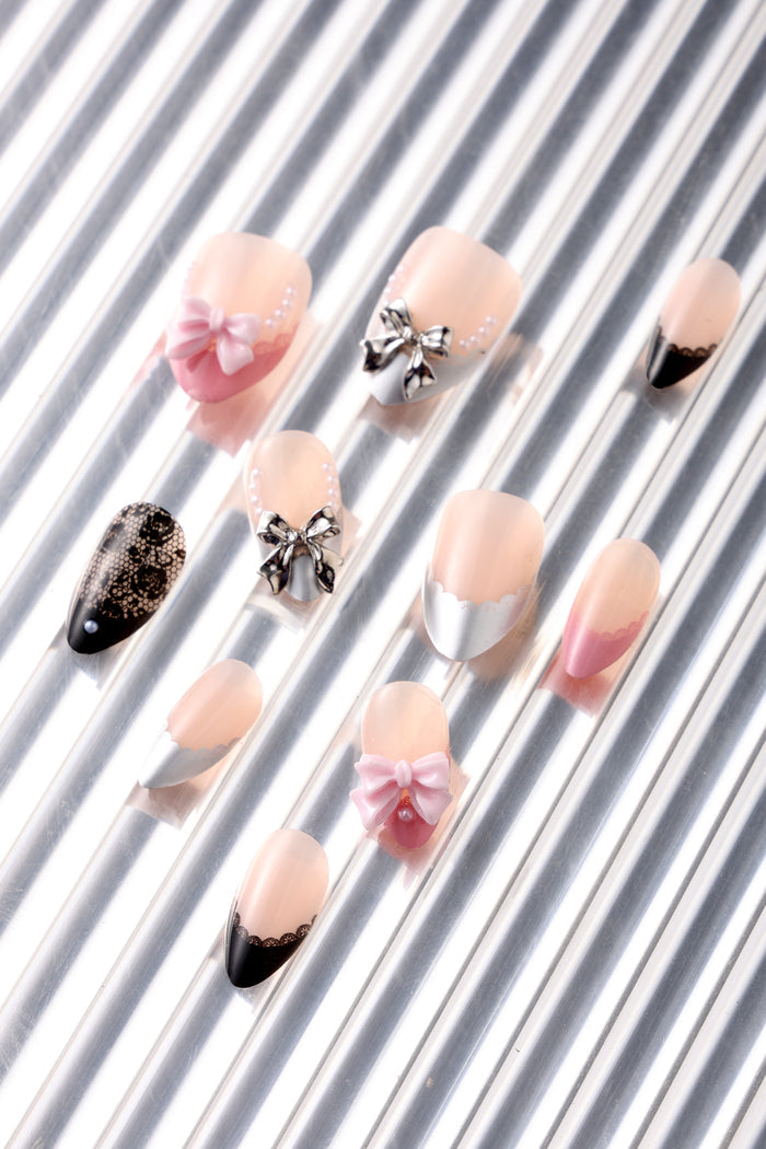 Short almond press-on nails with delicate lace, pink bows, and silver bows.